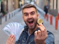 Mladý muž nadšeně drží bitcoinovou minci a hotovost, symbolizující rychlé zbohatnutí na kryptoměnách a příběhy některých raných investorů.
