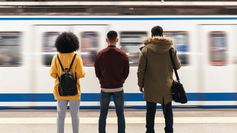 Three people waiting on the station as metro passes by.