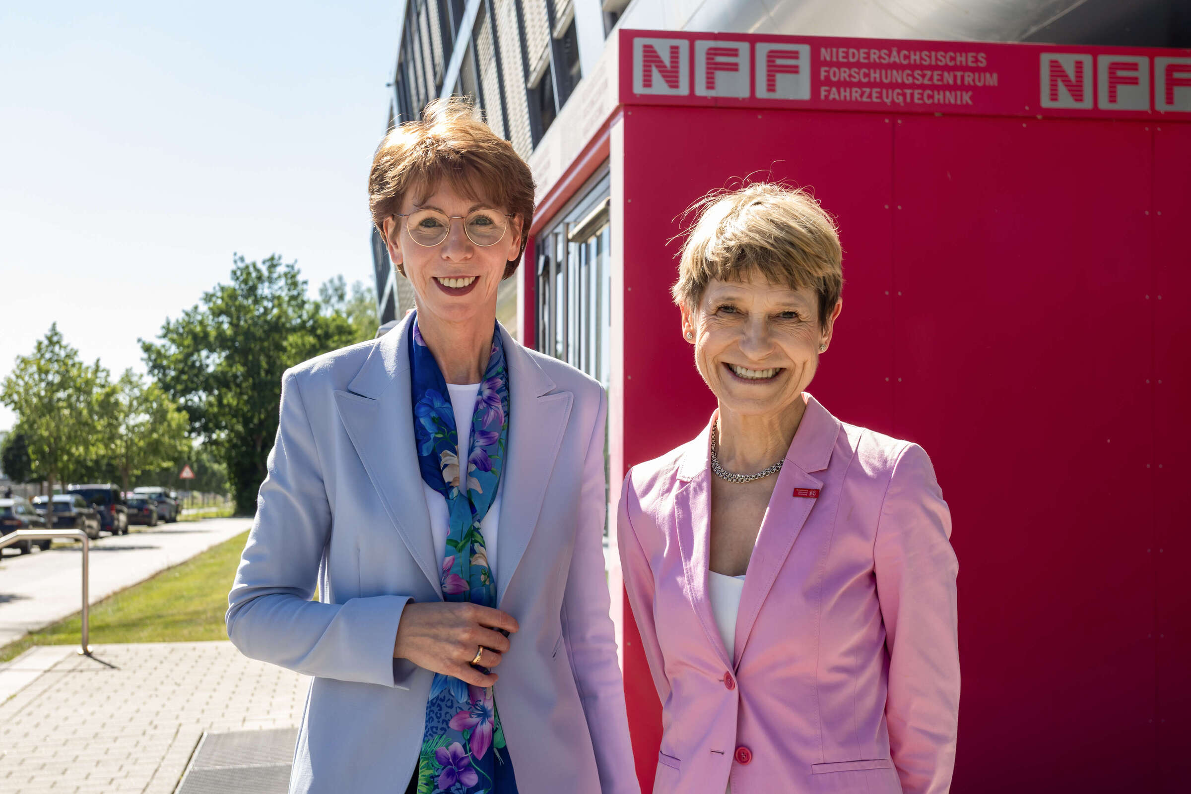 Two women in business attire smiling in front of a building with an NFF sign.