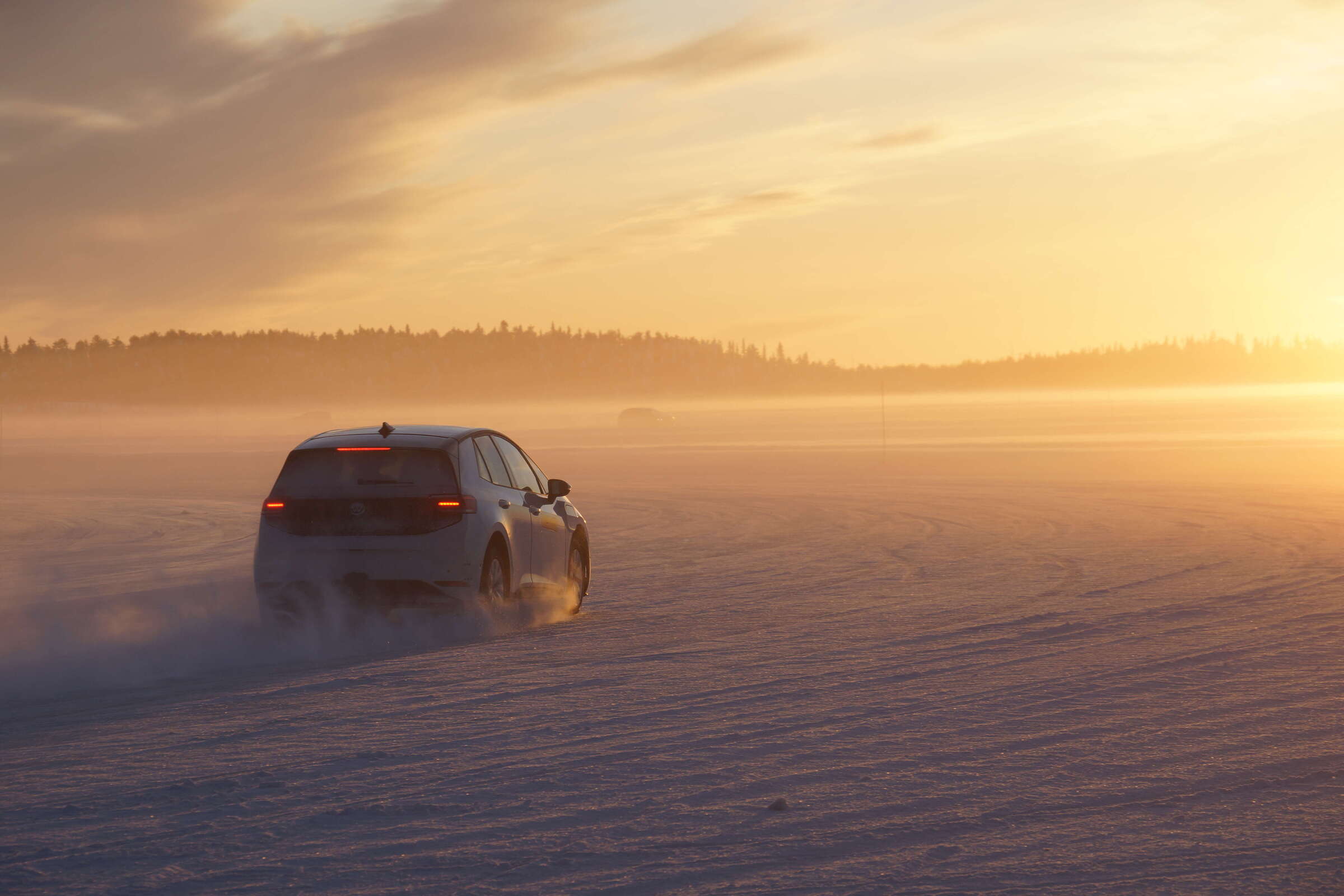 Car driving across a snowy plain in warm sunrise/sunset light, with mist on the horizon.