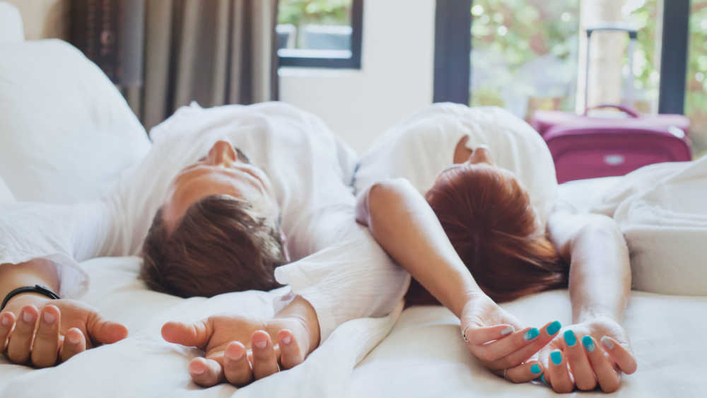 Two people stretching on a bed in their tourist accommodation.