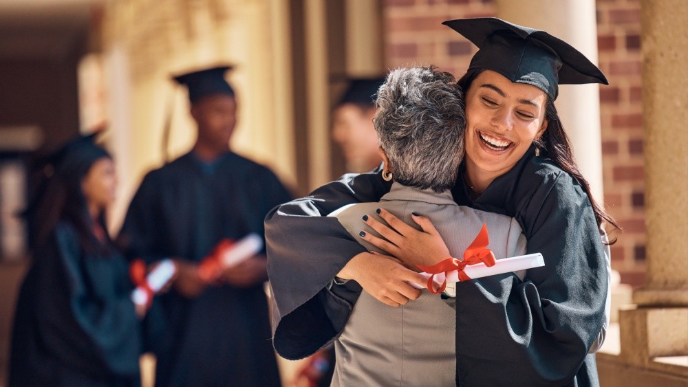 A young women celebrating graduation embraces an older women.