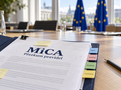 Ilustrativní obrázek dokumentu k přezkumu MiCA se záložkami DeFi, staking, lending a marketing na jednacím stole s vlajkami Evropské unie v pozadí. Vytvořeno pomocí AI.