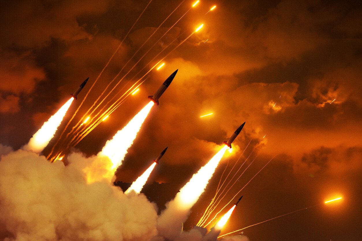 Dramatic night scene of a massive ballistic missile strike. Multiple rockets ascending through thick smoke and fire into a glowing orange sky. Concept of Middle East conflict, war, and escalation.