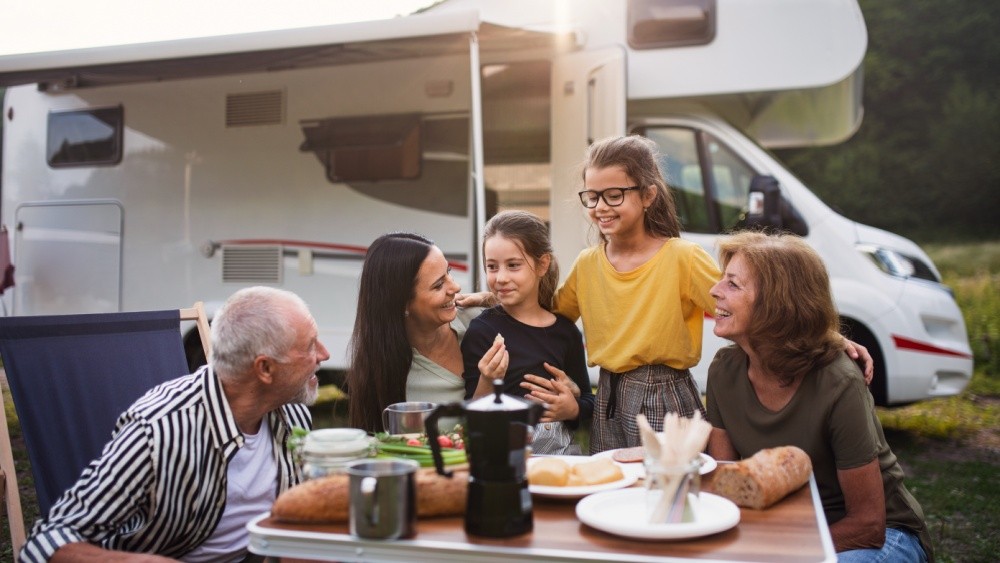 adults and children with adults around a table with food and a recreational vehicle in the background