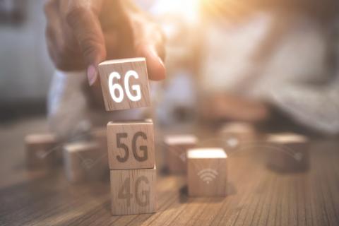 A person is building a tower of wooden blocks representing the evolution of mobile network technology, from 4G to 5G, and now to the future of 6G.