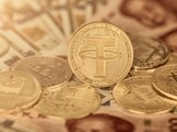 Zlatá mince s logem stablecoinu tether (USDT) uprostřed, obklopená dalšími kryptoměnami včetně bitcoinu, položená na bankovkách amerického dolaru a čínského jüanu. Symbolizuje rostoucí význam Tetheru a kryptoměn ve světové ekonomice.