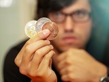 Muž drží mince symbolizující kryptoměny a zvažuje investiční možnosti.
