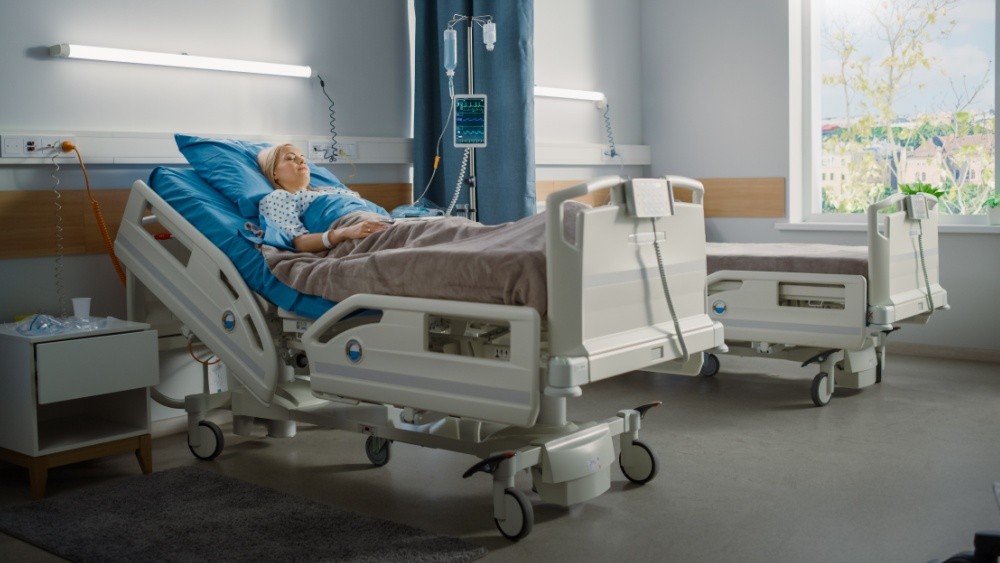 woman laying on hospital bed on an hospital room with an empty bed next to her.